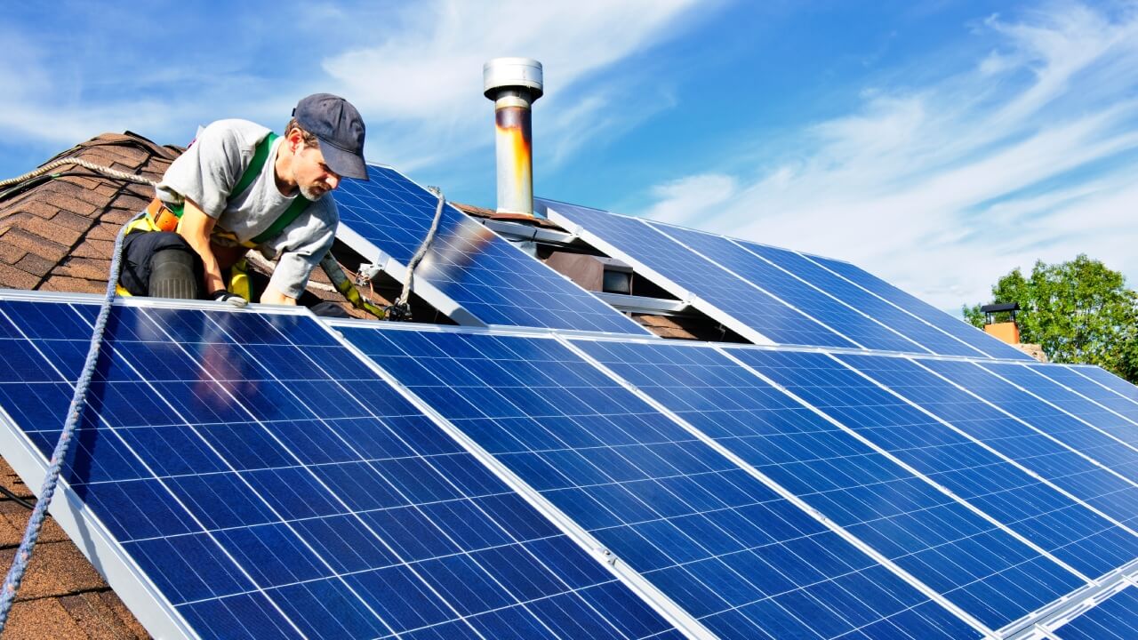Are solar panels worth it? A person on the roof of a house installing solar panels onto a rail.