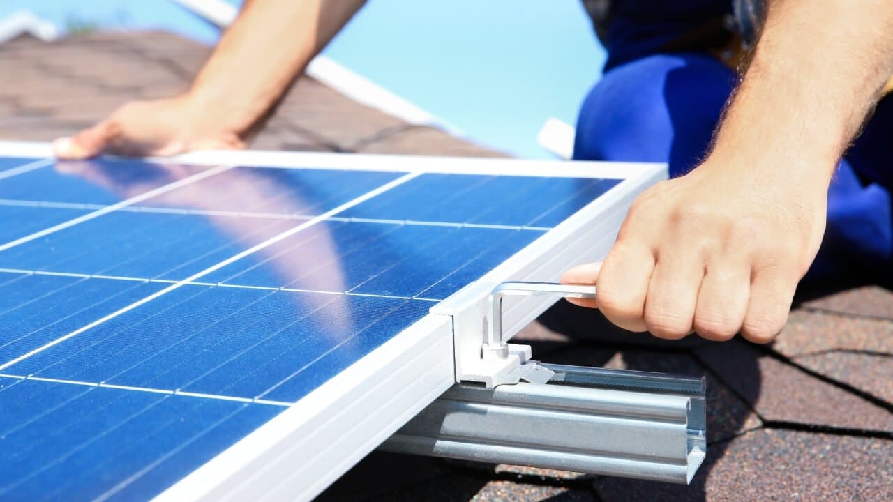 How solar panels are installed. A person using an allen key to fix a solar panel to a rail on the roof of a house.
