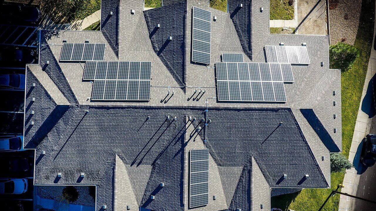 Solar panel grants. An aerial overhead view of a set of solar panels installed on the grey roof of a large building.